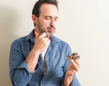 资深男士吃巧克力甜甜圈严肃的面孔思考问题, 非常困惑的想法照片