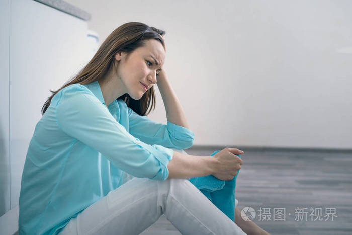 坐在厨房地板上的年轻女子抱着她的头, 哭着, 沮丧, 悲伤, 沮丧