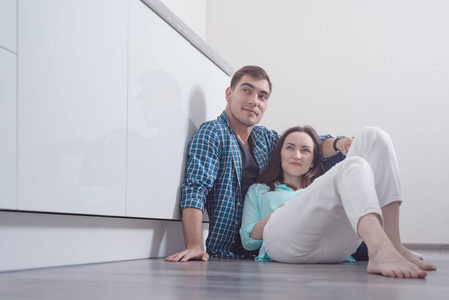 年轻夫妇坐在实木复合地板上的白色厨房的内部, 并期待在侧面, 复制空间