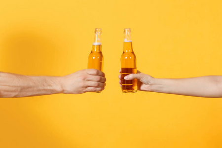 关闭妇女和男子手水平持有啤酒瓶隔离在黄色的背景。体育迷们为支持团队喝彩。体育家庭休闲生活方式概念