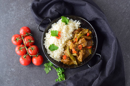 猪肉饭猪肉在辣咖喱汁与茄子和青豆,配上灰色的抽象背景黑色的金属碗