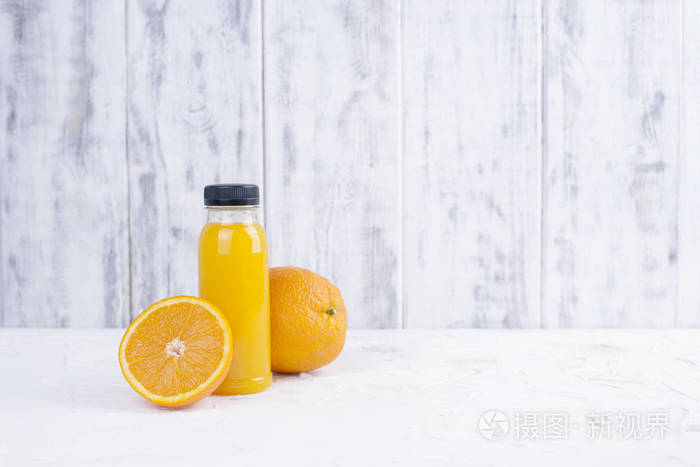 鲜艳的橘子和橙汁放在塑料瓶里。白色木质背景。复制空间