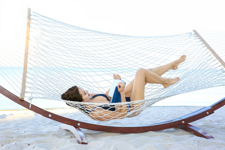 在海边的吊床上躺着书的年轻女子。暑假