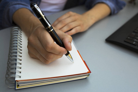 在笔记本上用钢笔写字的女人的手.现代灰色办公室书桌.