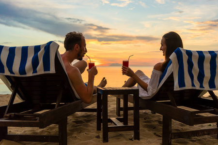 年轻夫妇在海滩上喝鸡尾酒在日落期间在假期