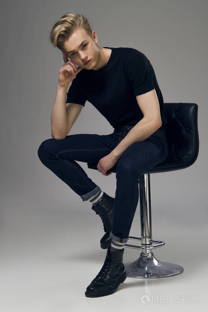 一个年轻的男模特,坐在椅子上的全长图片