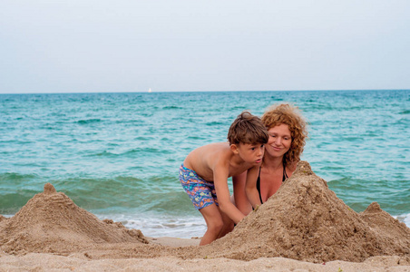 妈妈帮助儿子打造塔的海滩上的沙
