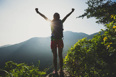 成功的女性徒步旅行者与 outstreched 胳膊站立在山顶在日出期间