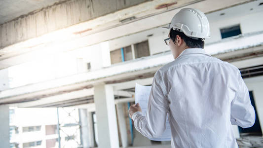 亚洲男性工程师或建筑师在施工现场佩戴防护安全帽时, 检查图纸或建筑图纸。工程建筑和建筑概念