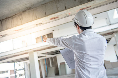 亚洲男性工程师或建筑师在施工现场佩戴防护安全帽时, 检查图纸或建筑图纸。工程建筑和建筑概念