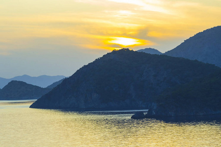地中海风景。日落在海面上, 阳光透过云层流动明亮的彩色射线。山脉的剪影。背景