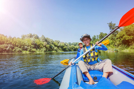 愉快的男孩独木舟在河上在阳光明媚的天在暑假期间