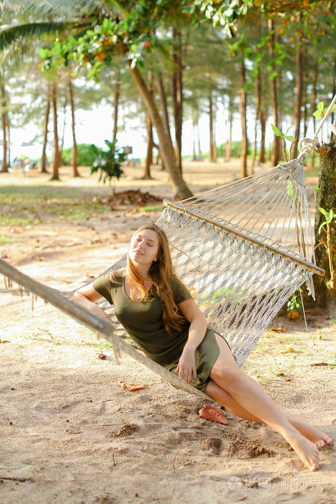 年轻女孩赤脚坐在柳条吊床, 沙子和树木背景