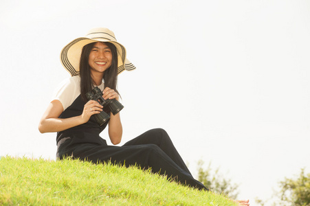 漂亮的亚洲年轻女子坐在土墩上寻找望远镜。