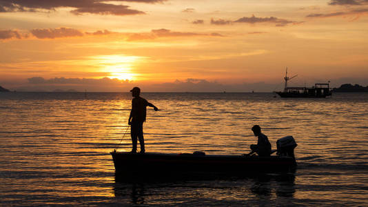 两个渔民在一艘小渔船舷外发动机上的海洋在夜幕降临的剪影