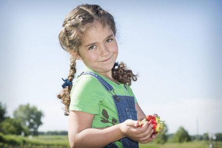 在夏天, 在花园里, 一个小, 金发, 卷发的女孩拿着草莓在她的手中