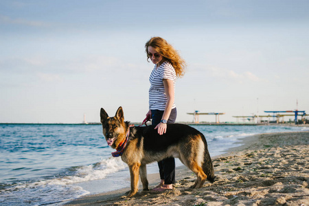 快乐的年轻女子步行与她的德国牧羊犬在海滩上户外