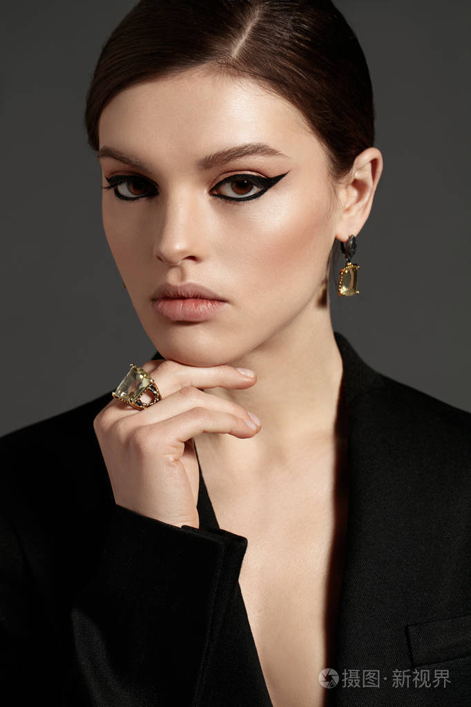 时尚肖像的年轻黑发模特与美丽化妆穿着时髦的耳环和戒指摆在灰色背景