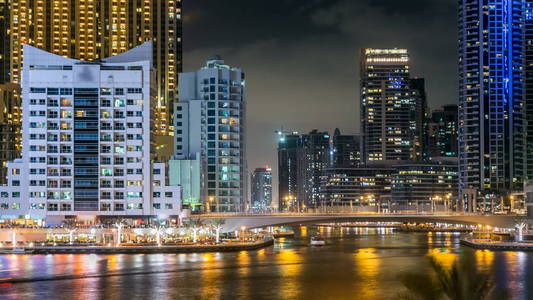 视图的迪拜码头长廊与船只, 棕榈和现代塔反映在水从路堤在迪拜夜 timelapse, 阿拉伯联合酋长国。迪拜码头是迪拜的一个地区