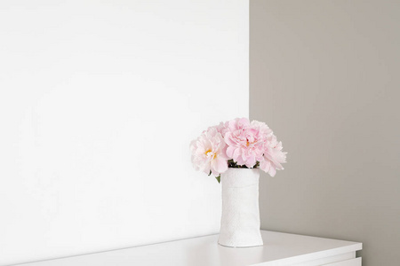 在房间的白色和灰色的墙壁的角度。在梳妆台上矗立着白色花瓶, 粉红色的花朵盛开着牡丹花。墙壁上涂有两种颜色。简单的简约内部。文本位