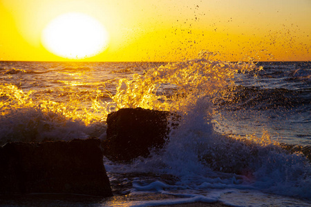 日落时美丽的大海。在黄色的太阳背景下喷洒和石头。海景
