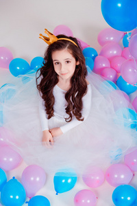 可爱的小公主女孩坐在房间里的气球在白色背景.看着照相机.童年照片