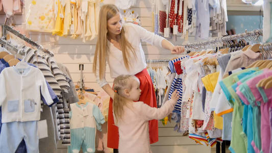 金发碧眼的年轻女子带着小女儿选择孩子穿的衣服店