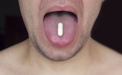 刮胡子的人拿着一块药片在他的舌头, 黑色背景, 特写