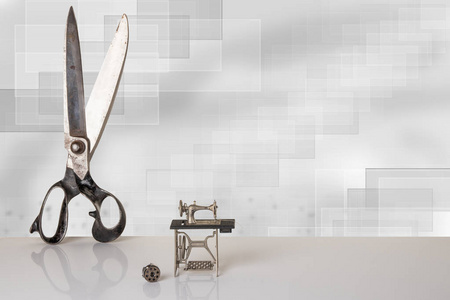 专业的老大裁缝剪刀和迷你模型的美丽复古缝纫机在白色的表与灰色的散景背景。广告为裁缝业务。文本和蒙太奇的空间