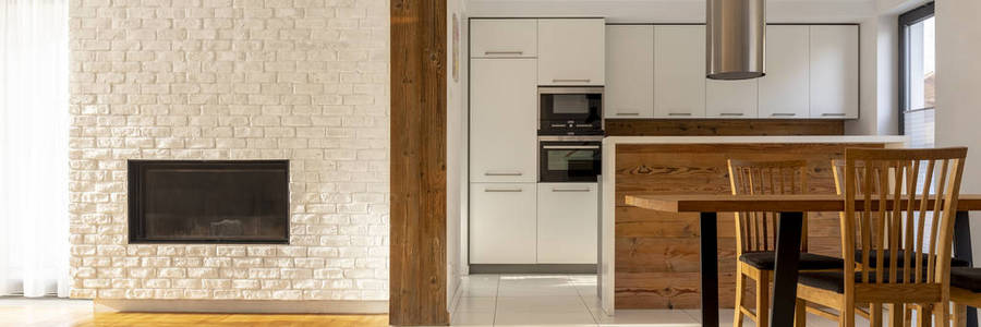 真正的照片白色开放空间厨房内部与两个烤箱, 木台面和餐桌上的椅子。壁炉上的墙壁上的空地方为您的电视