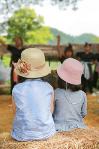 两个小女孩戴着帽子看着自然公园的文化表演的背面视图