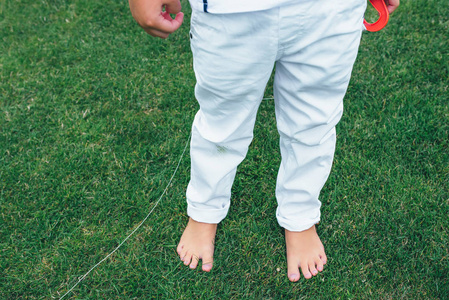 在白色牛仔裤的小男孩的腿.男孩正站在草地上.孩子的赤裸的双脚照片