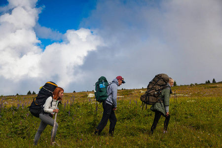 旅行生活方式和生存概念后视图。徒步旅行的妇女和男人带着背包享受着徒步旅行, 去山上, 在背景一片碧绿的田野, 群山中。阳光普照