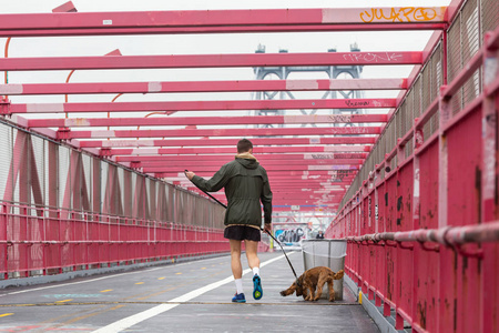 无法辨认的运动娱乐男性慢跑与他的狗在一个皮带在威廉斯堡大桥纽约市, 美国