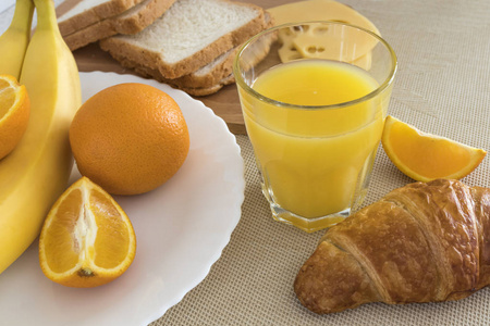 新鲜橙汁在玻璃烧杯, 牛角面包, 橙色切片, 香蕉, 奶酪, 面包。健康早餐