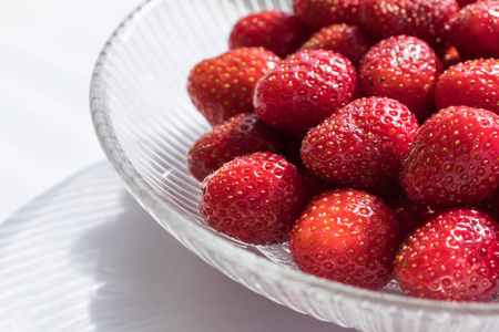 在一个白色的背景玻璃碗新鲜草莓。健康夏日甜点