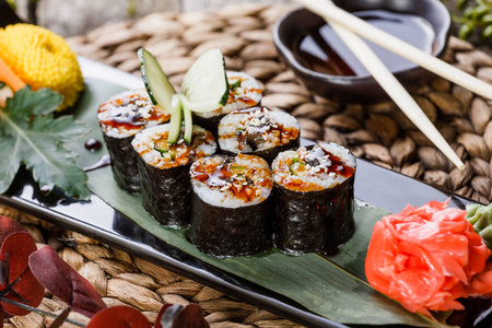 寿司卷Maki Sushi 与烟熏鳗鱼 黄瓜 鳄梨和芝麻上竹凉席用鲜花装饰的黑色石头上。日本料理