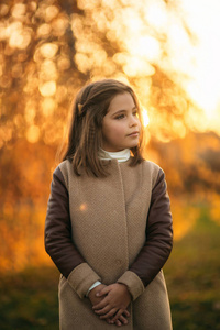 在秋天外套为摄影师摆姿势的小女孩。金色的秋天