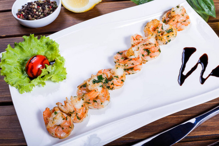 虾虾用酱油和青菜烤在木桌上的白色盘子上。海鲜美味佳肴