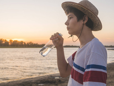 小男孩与瓶水站立在海滩在日落