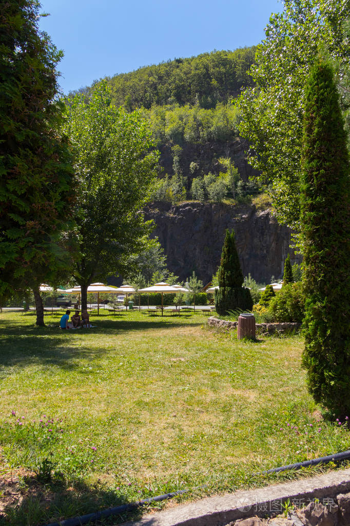 在悬崖脚下的树荫下, 年轻人正坐在草坪上的公园里.