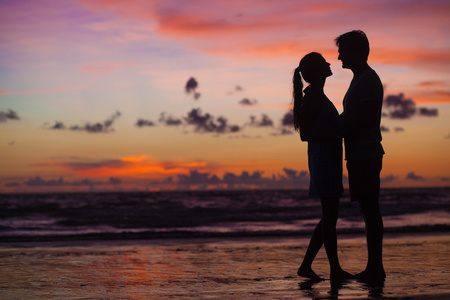 落日下的剪影的年轻夫妇在爱拥抱在海滩