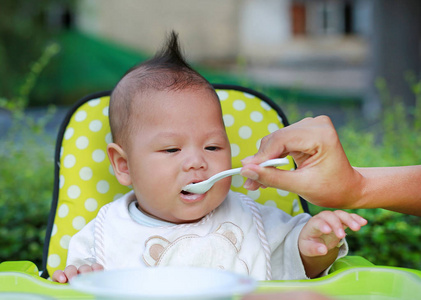 关闭婴儿婴儿的男孩在花园的椅子上喂养食物。婴儿第一次喂养食物