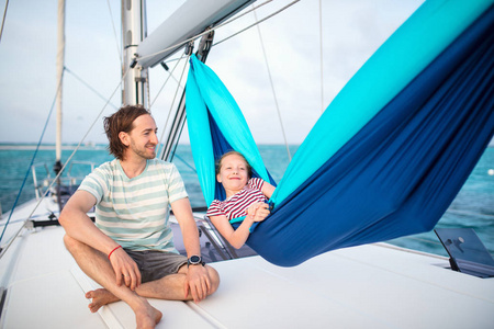 家庭的父亲和可爱的女孩放松在吊床上设置在风帆船上, 而在开阔的大海航行