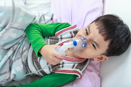 顶视图的愤怒的亚洲儿童持有面具蒸气吸入治疗哮喘照片