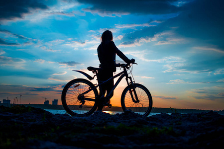 日落时带着自行车住在湖岸的年轻女子