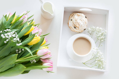 早餐一杯黑咖啡奶与糕点的柔和的颜色，在一束新鲜的黄色和粉红色郁金香，在白色背景上的春天。顶视图