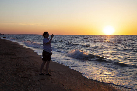 少年用照相机在日落的海