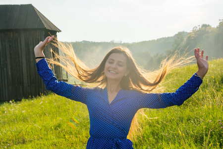 美丽的年轻女子是笑在阳光下的草地上的野花在老磨坊背景夏季