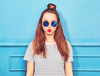 年轻时尚的女孩在休闲夏天的衣服, 红色的嘴唇, 摆在蓝色的墙壁附近的模型。膨化她的脸颊